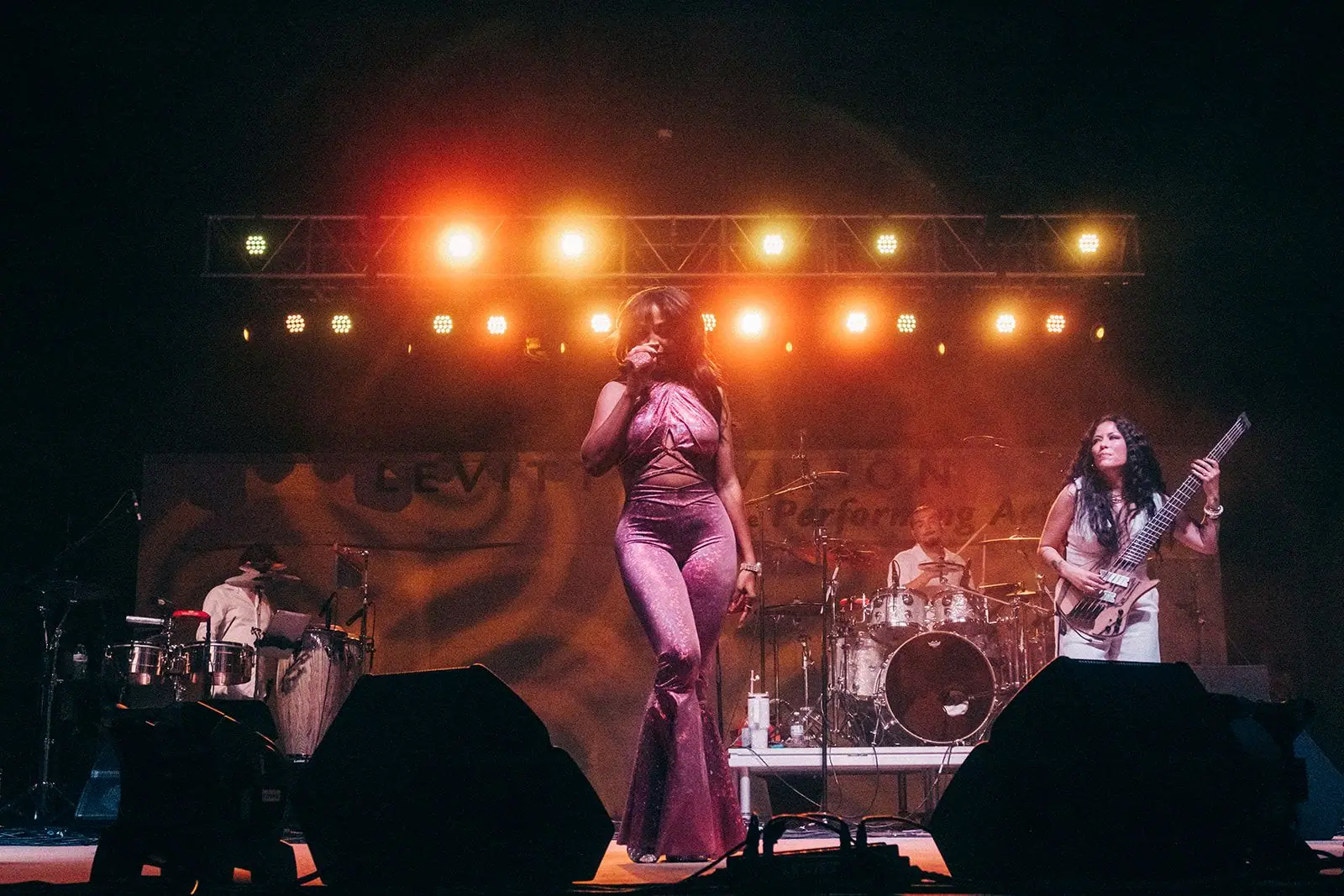 Tejano Queen Forever performs on stage under warm orange lighting, with a guitarist at right