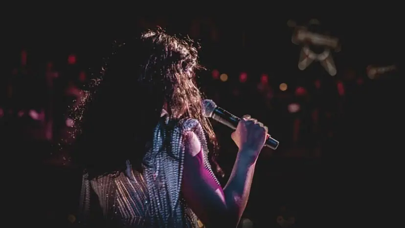 Carymel Rodríguez sings with her back to the camera, silhouetted against dim stage lights