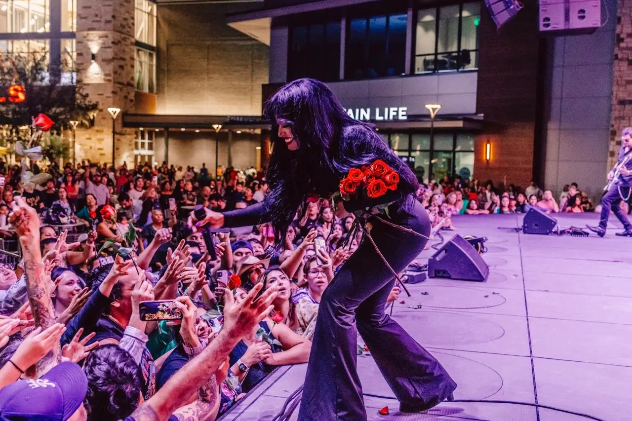 Carymel Rodríguez leans over the stage edge to fans, holding red roses