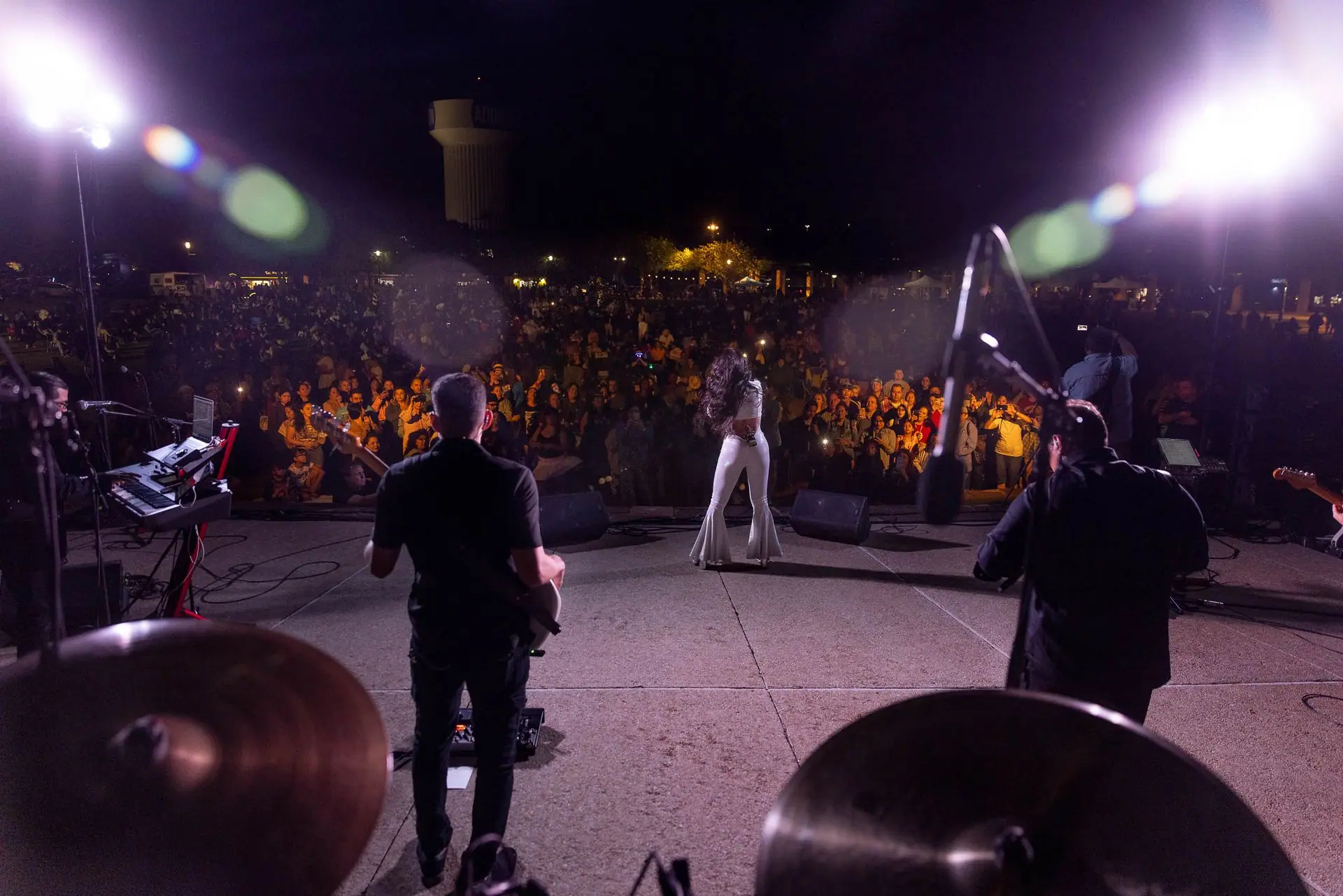 View from behind the drummer as the band plays an outdoor night show for a big crowd
