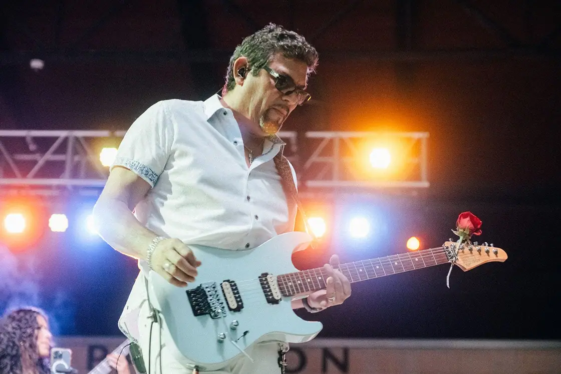 Chris Vasquez plays a white electric guitar with a red rose on the neck