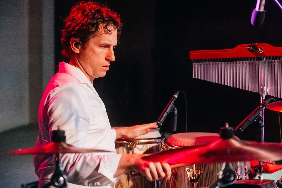 Mauricio Gutierrez Upmann plays percussion under red stage lights