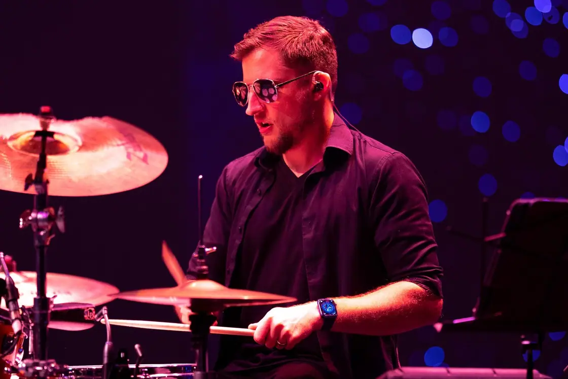 Mich Polan plays drums on stage in front of blue and purple lights