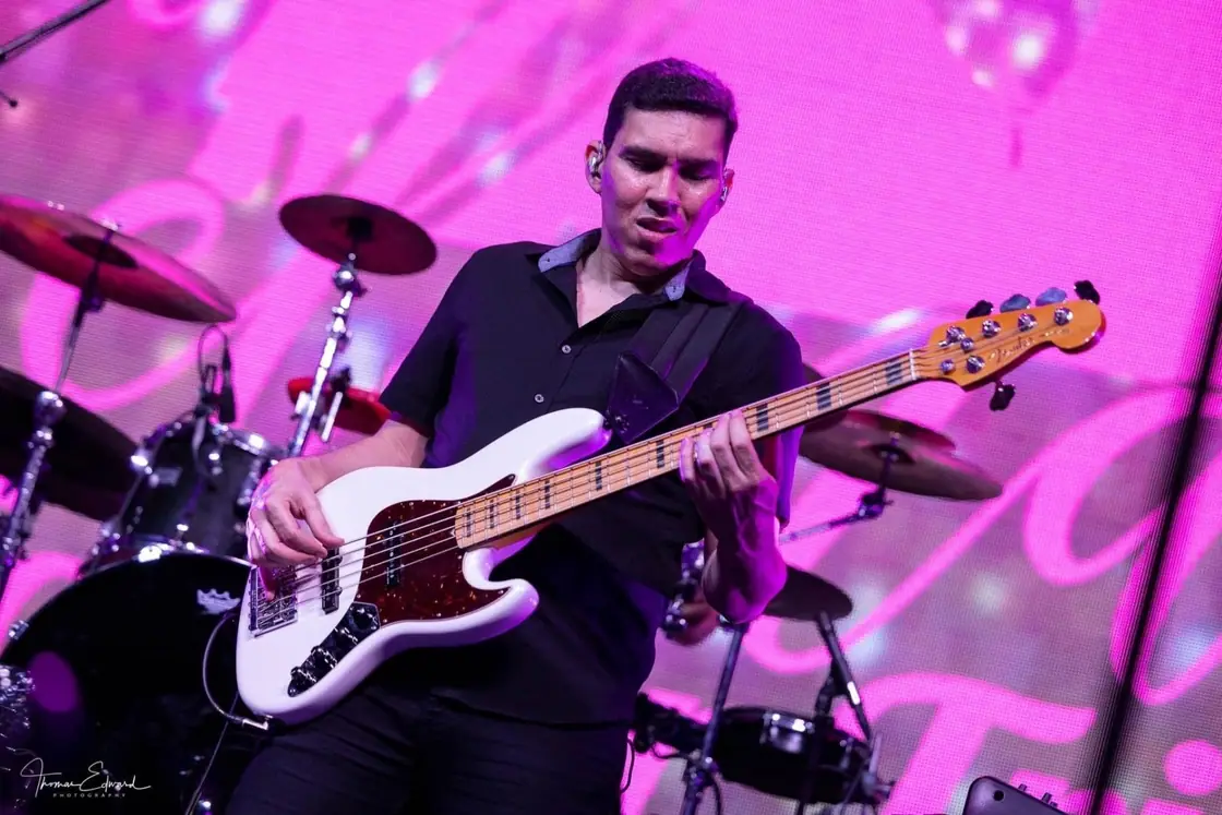 Nate Lima plays bass guitar on stage under bright pink lights