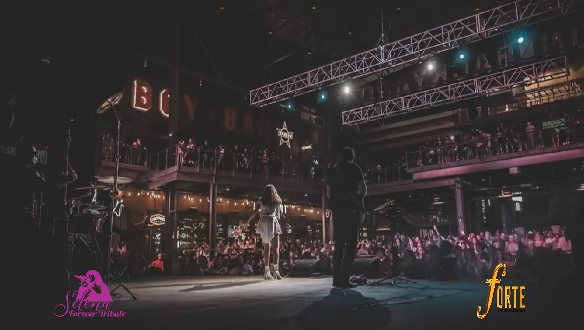 The band performs on an elevated stage as a large crowd watches from the balconies above