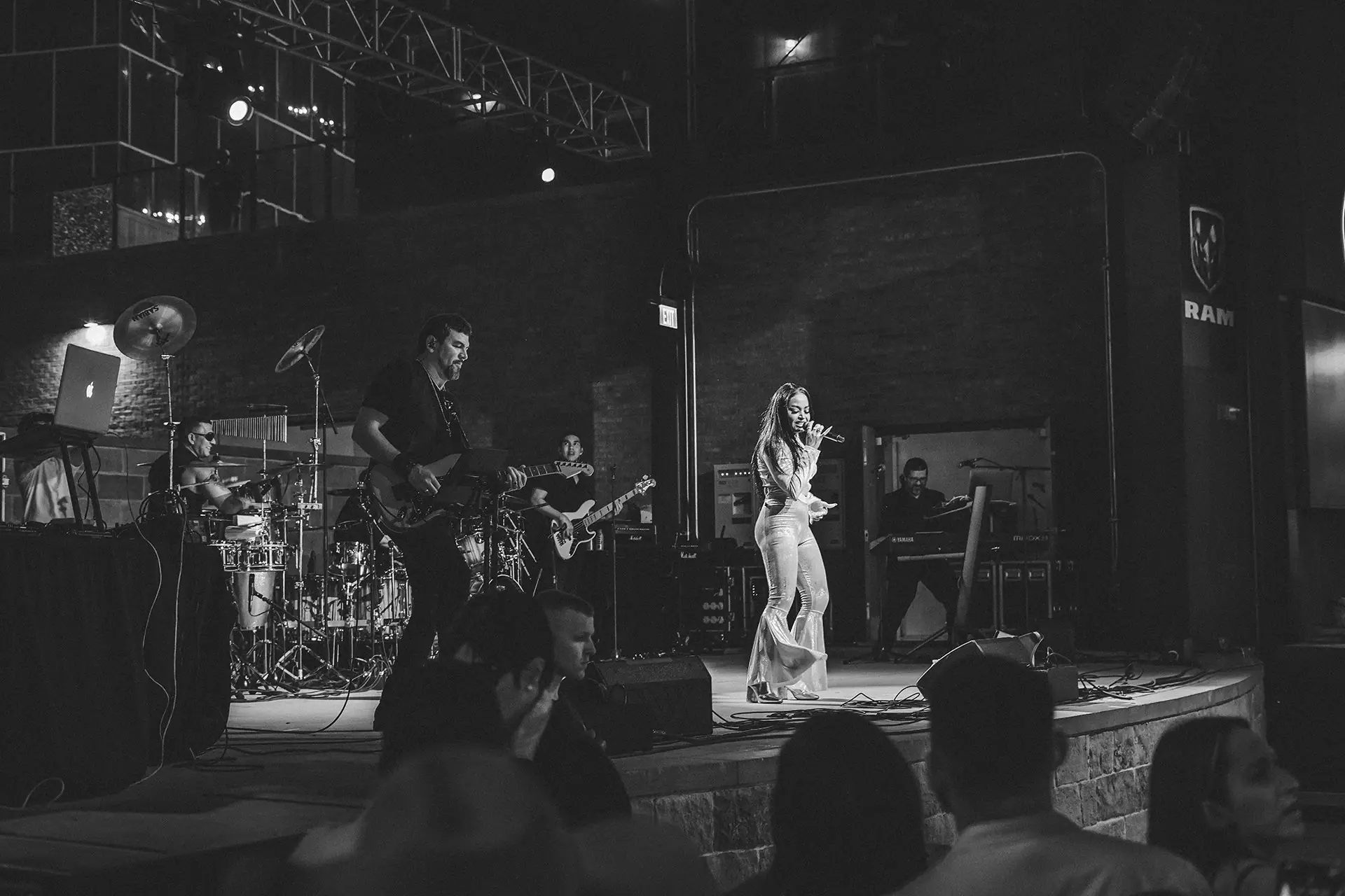 Black and white shot of the band on a covered stage, the singer in white at right, with the audience in the foreground